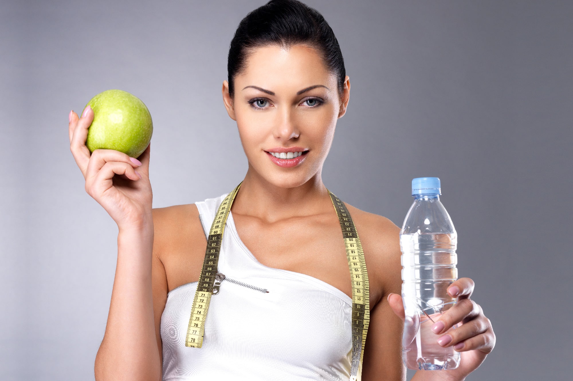 אישה מחזיקה בקבוק מים ותפוח ועל הצוור שלה סרט מדידה