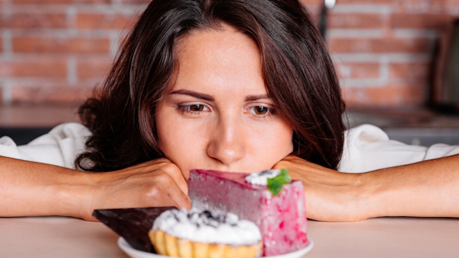 אישה בדיאטה משתוקקת לאכול עוגה יושבת על המטבח